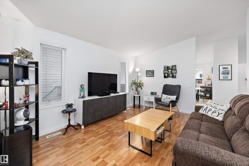 Bright living area featuring wood-finish flooring, white walls, and a large window with blinds - 3344 24 Avenue Nw, Edmonton, AB - Indoor Photo Showing Living Room