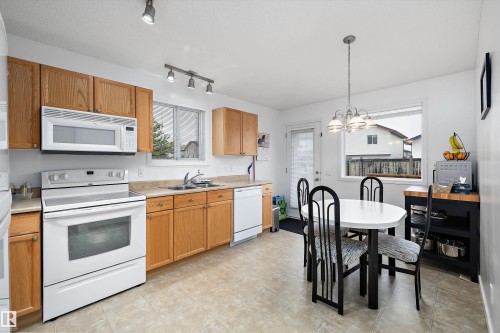 Kitchen featuring wood cabinetry, white appliances, a double basin sink, and a tiled floor - 3344 24 Avenue Nw, Edmonton, AB - Indoor Photo Showing Kitchen With Double Sink