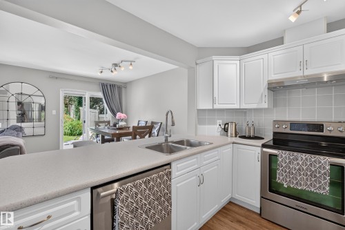 White cabinetry, grey tiled backsplash, stainless steel appliances, dual basin sink, and light-toned countertop - #25 200 Erin Ridge Dr, St. Albert, AB - Indoor Photo Showing Kitchen With Double Sink