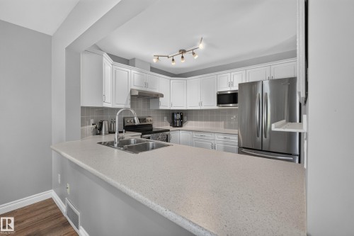 Kitchen featuring white cabinetry, light-toned countertops, tile backsplash, and stainless steel appliances - #25 200 Erin Ridge Dr, St. Albert, AB - Indoor Photo Showing Kitchen With Double Sink