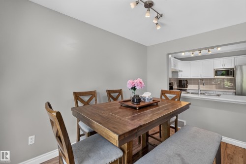 Open pass-through window to the kitchen, track lighting, wood-finish flooring, white baseboards, and light gray walls - #25 200 Erin Ridge Dr, St. Albert, AB - Indoor Photo Showing Dining Room