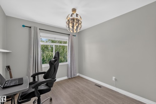 Modern home office featuring warm wood-finish flooring, soft gray walls, and abundant natural light from expansive glass doors and windows - #25 200 Erin Ridge Dr, St. Albert, AB - Indoor Photo Showing Office