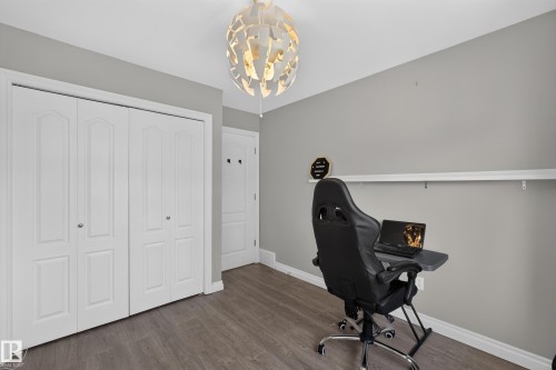 Modern home office featuring wood-finish flooring, soft gray walls with coordinating trim, abundant natural light from recessed ceiling fixtures, and ample wall space ideal for storage or display - #25 200 Erin Ridge Dr, St. Albert, AB - Indoor Photo Showing Other Room