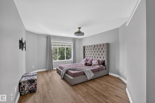 Spacious bedroom featuring wood-finish flooring, soft neutral wall finishes, and a tufted upholstered headboard - #25 200 Erin Ridge Dr, St. Albert, AB - Indoor Photo Showing Bedroom