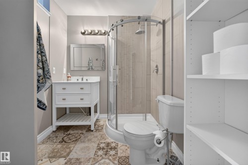 Vanity with integrated sink, patterned floor tile, enclosed shower with glass door, wall-mounted light fixture, and built-in shelving - #25 200 Erin Ridge Dr, St. Albert, AB - Indoor Photo Showing Bathroom
