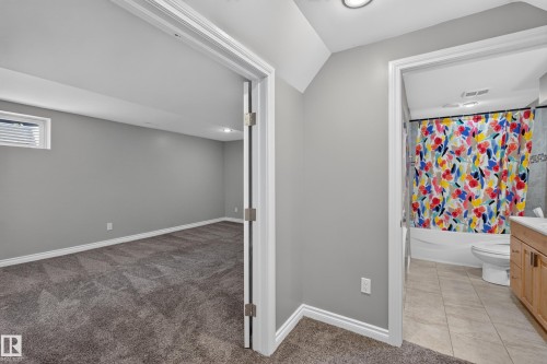 Primary suite bathroom featuring a colorful patterned shower curtain, wood-finish vanity with integrated storage, ceramic tile flooring, and soft overhead lighting - #25 200 Erin Ridge Dr, St. Albert, AB - Indoor Photo Showing Other Room