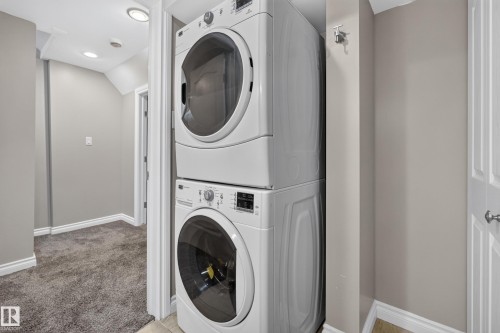 Stackable washer and dryer unit, recessed lighting, and soft gray wall paint in a dedicated utility space - #25 200 Erin Ridge Dr, St. Albert, AB - Indoor Photo Showing Laundry Room