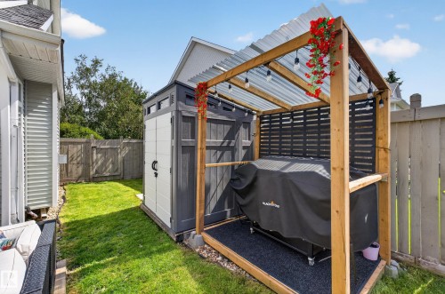 Manicured lawn, wood fencing, outdoor storage shed, wood-framed pergola with transparent corrugated roof, and string lighting - #25 200 Erin Ridge Dr, St. Albert, AB - Outdoor With Exterior