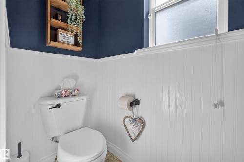 Powder room featuring white beadboard wainscoting, a white porcelain toilet with chrome hardware, and navy blue walls above the chair rail - #25 200 Erin Ridge Dr, St. Albert, AB - Indoor Photo Showing Bathroom