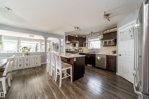 Kitchen featuring dark wood-finish cabinetry, stainless steel appliances, a center island with countertop seating, and wood-finish flooring - 7239 21 Avenue Sw, Edmonton, AB - Indoor Photo Showing Kitchen With Upgraded Kitchen