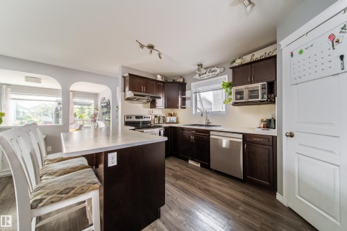 Kitchen featuring wood-finish flooring, dark wood cabinetry, light countertops, and stainless steel appliances - 7239 21 Avenue Sw, Edmonton, AB - Indoor Photo Showing Kitchen