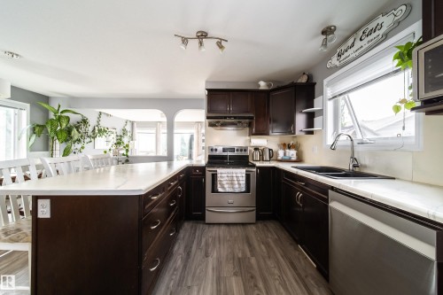 Contemporary kitchen featuring dark cabinetry, stainless steel appliances, white quartz countertops, a large center island with seating, and wood-finish flooring throughout - 7239 21 Avenue Sw, Edmonton, AB - Indoor Photo Showing Kitchen With Double Sink
