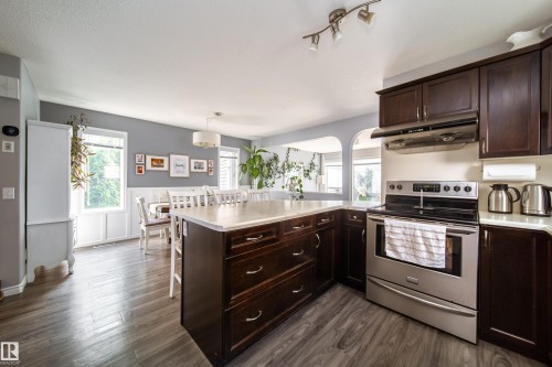Kitchen featuring dark wood-finish cabinetry, stainless steel range with hood, and a light-toned countertop - 7239 21 Avenue Sw, Edmonton, AB - Indoor Photo Showing Kitchen