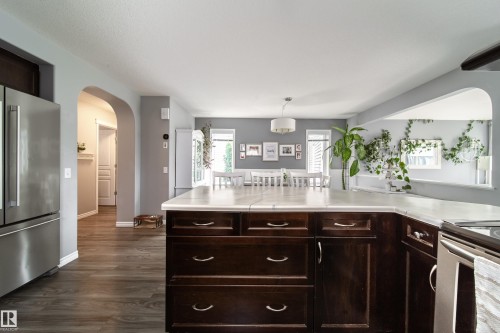 Kitchen featuring dark wood-finish cabinetry, light-toned countertops, and stainless steel appliances - 7239 21 Avenue Sw, Edmonton, AB - Indoor Photo Showing Kitchen