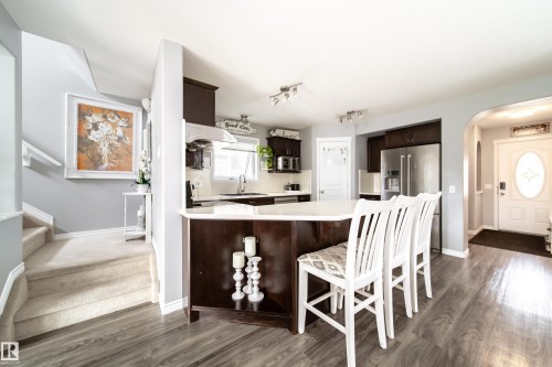 Modern kitchen with dark wood-finish cabinetry, stainless steel appliances, and a white countertop island - 7239 21 Avenue Sw, Edmonton, AB - Indoor
