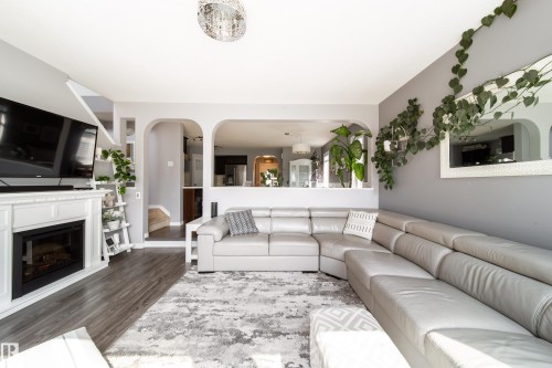 White mantel fireplace with an electric insert, wood-finish flooring, and arched doorways - 7239 21 Avenue Sw, Edmonton, AB - Indoor Photo Showing Living Room With Fireplace