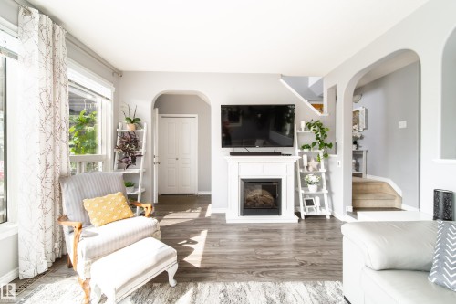 Living area featuring wood-finish flooring, a white fireplace with an electric insert, and large windows - 7239 21 Avenue Sw, Edmonton, AB - Indoor Photo Showing Living Room With Fireplace