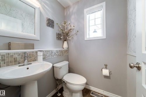 Powder room featuring a pedestal sink with chrome fixtures, ceramic tile backsplash in neutral tones, toilet with dual-flush capability, and recessed lighting - 7239 21 Avenue Sw, Edmonton, AB - Indoor Photo Showing Bathroom