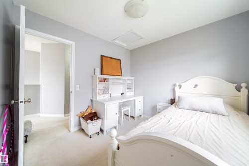 Bright secondary bedroom featuring soft gray walls, carpeted flooring, and a white curved-headboard bed with white bedding - 7239 21 Avenue Sw, Edmonton, AB - Indoor Photo Showing Bedroom
