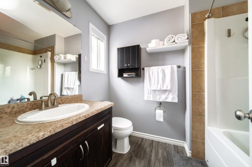 Spa-inspired bathroom featuring a dark cabinetry vanity with stone-finish countertop, oval undermount sink, and chrome faucet - 7239 21 Avenue Sw, Edmonton, AB - Indoor Photo Showing Bathroom