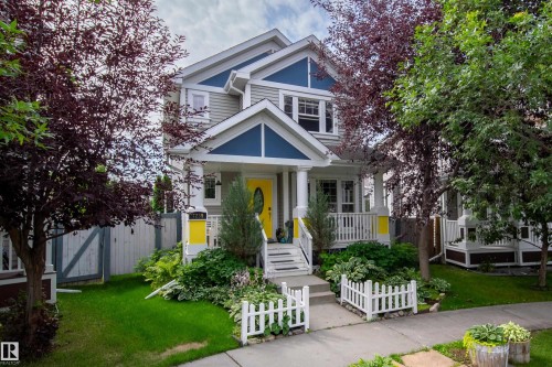 Two-story residence featuring a covered front porch with white railings, a vibrant yellow front door, and a manicured front lawn - 7239 21 Avenue Sw, Edmonton, AB - Outdoor With Deck Patio Veranda With Facade