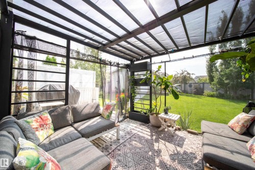 Modern conservatory with polycarbonate roof panels and black aluminum framing, featuring comfortable seating areas, potted greenery, geometric patterned area rug, and direct access to expansive manicured lawn with mature trees and open grounds beyond - 7239 21 Avenue Sw, Edmonton, AB -  Photo Showing Other Room