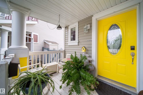 Inviting front porch with a bright yellow oval-lite entry door, white columns, and wood plank flooring - 7239 21 Avenue Sw, Edmonton, AB - Outdoor With Deck Patio Veranda With Exterior