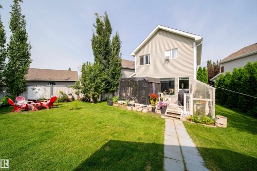 Expansive backyard featuring a green lawn, mature trees, a concrete pathway, a wooden deck, and a screened patio area - 7239 21 Avenue Sw, Edmonton, AB - Outdoor