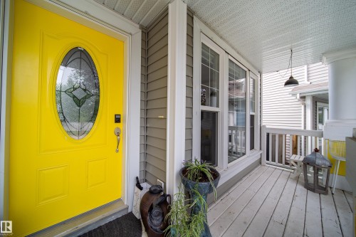 Front entry featuring a bright yellow door with decorative oval glass insert, a covered porch with white wood-finish flooring, and horizontal siding - 7239 21 Avenue Sw, Edmonton, AB - Outdoor With Deck Patio Veranda With Exterior