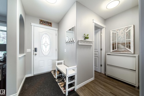 Entryway featuring a decorative front door with an oval glass insert, wood-finish flooring, a wall niche, and an overhead flush-mount light fixture - 7239 21 Avenue Sw, Edmonton, AB - Indoor Photo Showing Other Room