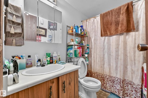 Bathroom featuring a wood-finish vanity with a white countertop and integrated sink, a mirrored medicine cabinet, and a white toilet - #206 10842 107 St Nw, Edmonton, AB - Indoor Photo Showing Bathroom