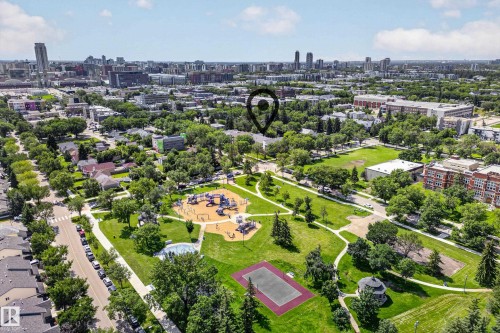Aerial view of a vibrant residential community featuring expansive green spaces, mature landscaping, multiple recreational facilities including a playground with equipment, sports courts, and manicured lawns - #206 10842 107 St Nw, Edmonton, AB - Outdoor With View