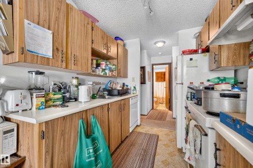 Kitchen featuring wood-finish cabinetry, white countertops, a white built-in dishwasher, and a white refrigerator - #206 10842 107 St Nw, Edmonton, AB - Indoor Photo Showing Kitchen