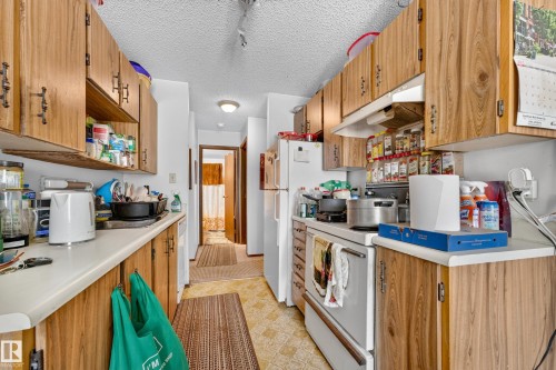 Galley kitchen featuring wood-finish cabinetry, white countertops, and patterned vinyl flooring - #206 10842 107 St Nw, Edmonton, AB - Indoor Photo Showing Kitchen