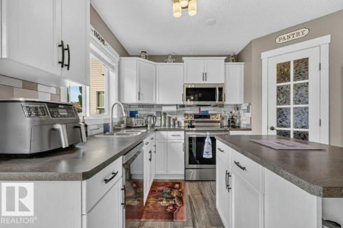 Kitchen featuring white shaker-style cabinetry, dark countertops, and stainless steel appliances - 5322 Terwillegar Boulevard Nw, Edmonton, AB - Indoor Photo Showing Kitchen