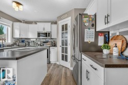 Kitchen featuring white cabinetry, dark countertops, wood-finish flooring, stainless steel appliances, and a glass-paneled pantry door - 