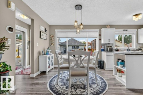 Open-concept dining area featuring wood-finish flooring, a contemporary triple pendant light fixture, and a large window providing natural illumination - 5322 Terwillegar Boulevard Nw, Edmonton, AB - Indoor