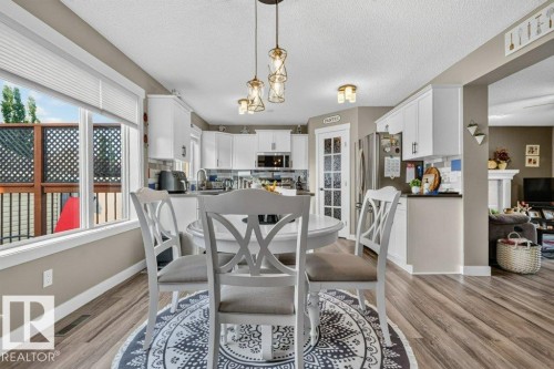 Open concept dining area with wood-finish flooring, featuring a large window with privacy blinds, and decorative pendant lighting - 5322 Terwillegar Boulevard Nw, Edmonton, AB - Indoor Photo Showing Dining Room