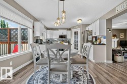 Open concept dining area with wood-finish flooring, featuring a large window with privacy blinds, and decorative pendant lighting - 