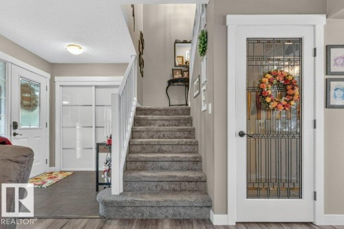 Carpeted staircase with white railing, wood-finish flooring, and a white door with decorative glass panels - 5322 Terwillegar Boulevard Nw, Edmonton, AB - Indoor Photo Showing Other Room