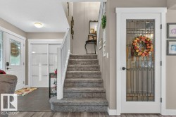 Carpeted staircase with white railing, wood-finish flooring, and a white door with decorative glass panels - 