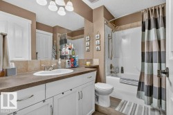 Bathroom featuring a white vanity with panel cabinetry and brushed nickel hardware, a dark countertop, a large mirror, a tile backsplash, and a tub/shower combination with a tile surround - 