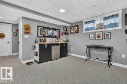 Basement recreation space featuring a built-in wet bar with a light wood-finish countertop, dark cabinetry, and a stainless steel undercounter refrigerator - 