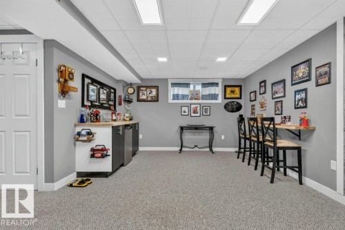 Finished lower level featuring a built-in wet bar with dual beverage refrigerators, drop ceiling with recessed lighting, wall-mounted bar table with stools, and neutral-toned carpeting throughout - 5322 Terwillegar Boulevard Nw, Edmonton, AB - Indoor