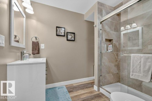 Bathroom featuring a glass-enclosed shower with tile surround and built-in niche, a white vanity with integrated sink, and wood-finish flooring - 5322 Terwillegar Boulevard Nw, Edmonton, AB - Indoor Photo Showing Bathroom