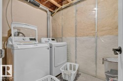 Dedicated laundry area featuring a top-loading washer and front-loading dryer, exposed overhead beams, and partial wall insulation - 