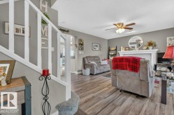 Living area featuring wood-finish flooring, a ceiling fan with integrated lighting, and a white mantelpiece - 