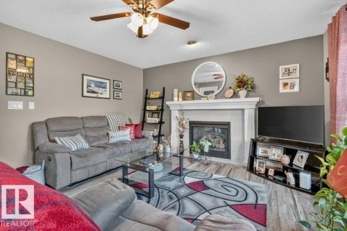Living area featuring a fireplace with a white mantel, neutral wall tones, wood-finish flooring, and a ceiling fan with integrated lighting - 5322 Terwillegar Boulevard Nw, Edmonton, AB - Indoor Photo Showing Living Room With Fireplace