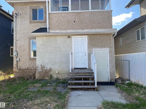 Stucco exterior with multiple entry points, featuring a second-story enclosed balcony, ground-level access, and a chain-link fence - 11029 95 Street Nw, Edmonton, AB - Outdoor With Exterior