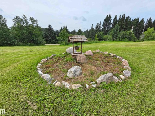 Expansive lawn with a decorative wishing well feature, bordered by natural stones, and surrounded by mature trees - Rural St. Paul County, AB 
